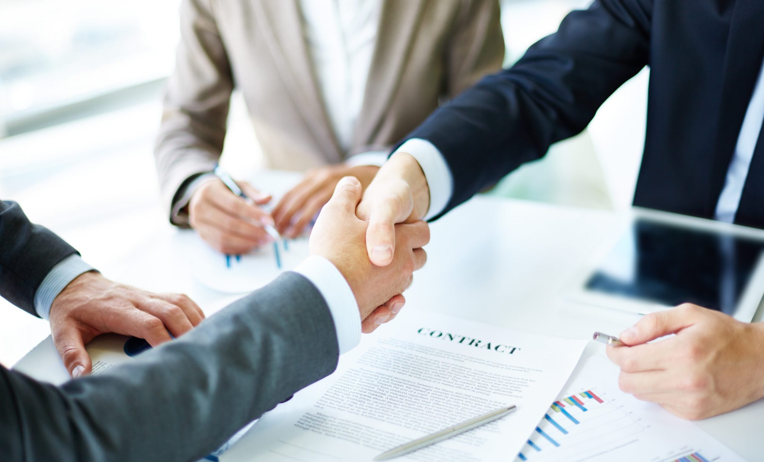 Making agreement Image of business partners handshaking over business objects on workplace